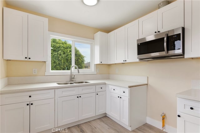 kitchen with light wood-type flooring, white cabinetry, and sink