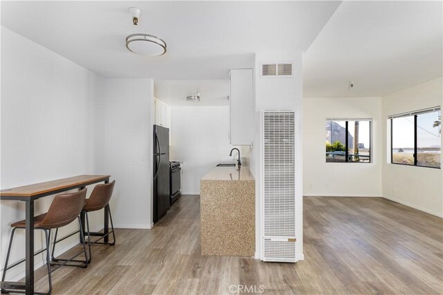 kitchen with white cabinetry, light hardwood / wood-style floors, black fridge, and sink