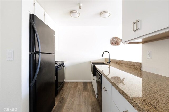 kitchen featuring appliances with stainless steel finishes, white cabinetry, light stone counters, dark hardwood / wood-style floors, and sink