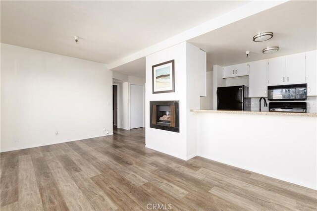 kitchen featuring white cabinets, a fireplace, black appliances, light hardwood / wood-style flooring, and sink