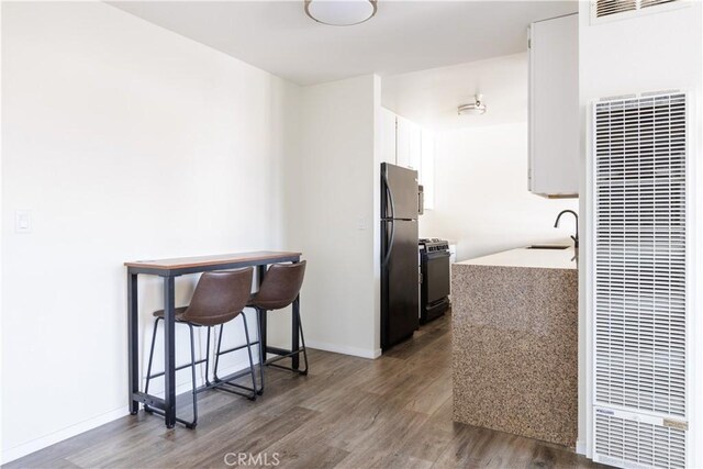 kitchen featuring stainless steel fridge, black gas range oven, dark wood-type flooring, white cabinets, and sink