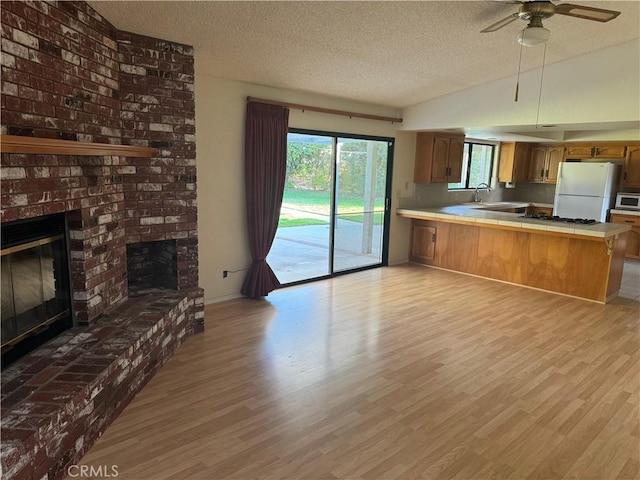 kitchen with kitchen peninsula, light wood-type flooring, white appliances, and a fireplace