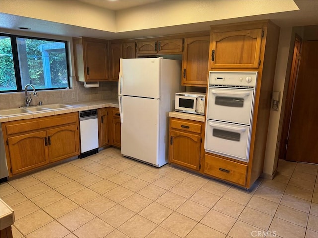 kitchen featuring tasteful backsplash, sink, light tile patterned flooring, and white appliances