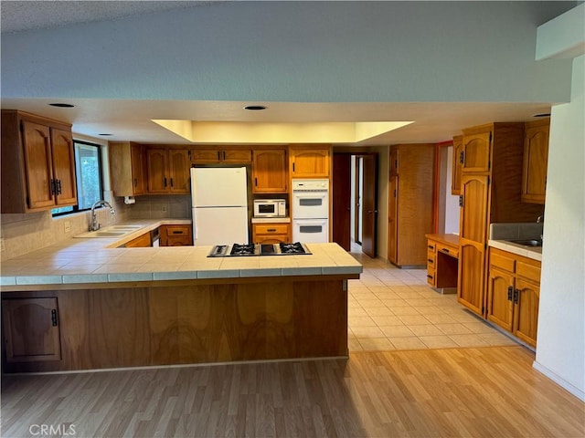 kitchen featuring kitchen peninsula, white appliances, sink, light hardwood / wood-style floors, and tile counters