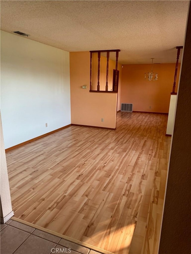 empty room featuring light hardwood / wood-style floors, a textured ceiling, and a chandelier