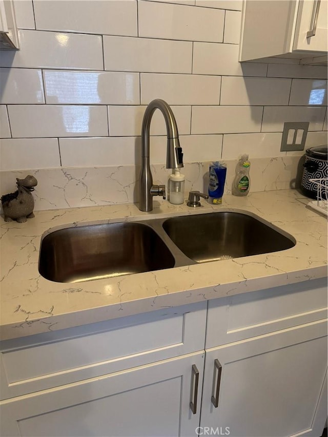 details with white cabinetry, light stone countertops, sink, and tasteful backsplash