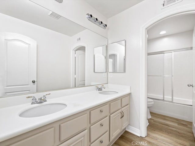 full bathroom featuring wood-type flooring, combined bath / shower with glass door, vanity, and toilet