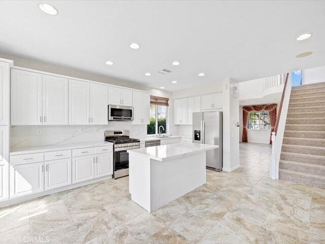 kitchen with tasteful backsplash, sink, white cabinets, appliances with stainless steel finishes, and a center island