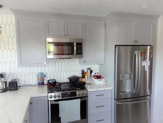 kitchen with light stone counters, backsplash, and appliances with stainless steel finishes