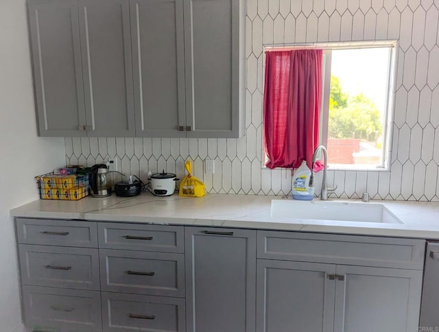 kitchen with decorative backsplash, gray cabinets, white dishwasher, and sink