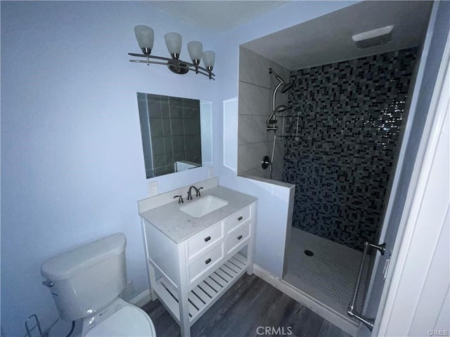 bathroom with hardwood / wood-style flooring, vanity, toilet, and tiled shower