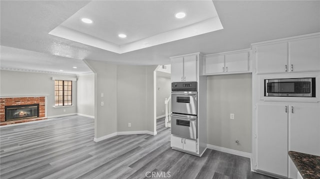 kitchen featuring a raised ceiling, hardwood / wood-style flooring, a fireplace, white cabinetry, and stainless steel appliances