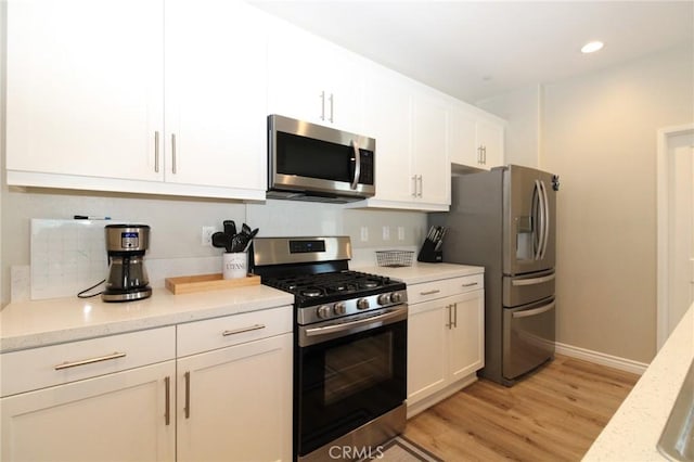 kitchen with light stone countertops, white cabinets, stainless steel appliances, and light wood-type flooring