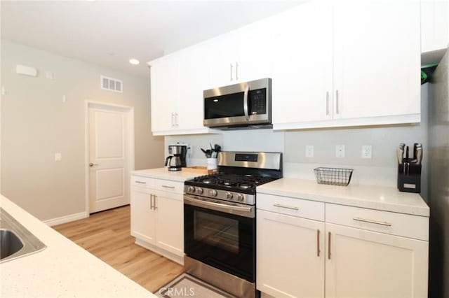 kitchen with appliances with stainless steel finishes, light hardwood / wood-style floors, and white cabinetry