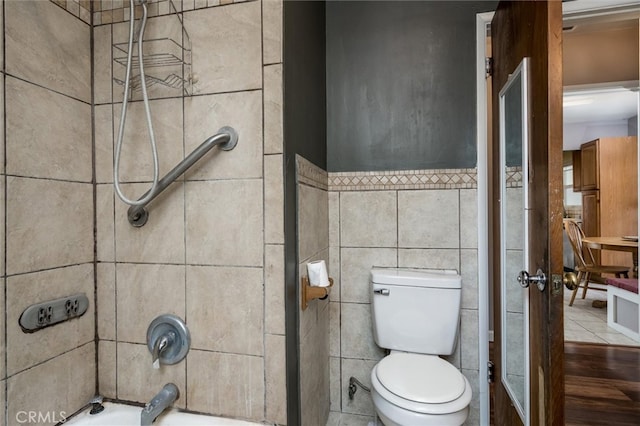 bathroom with tile walls, tiled shower / bath combo, and toilet