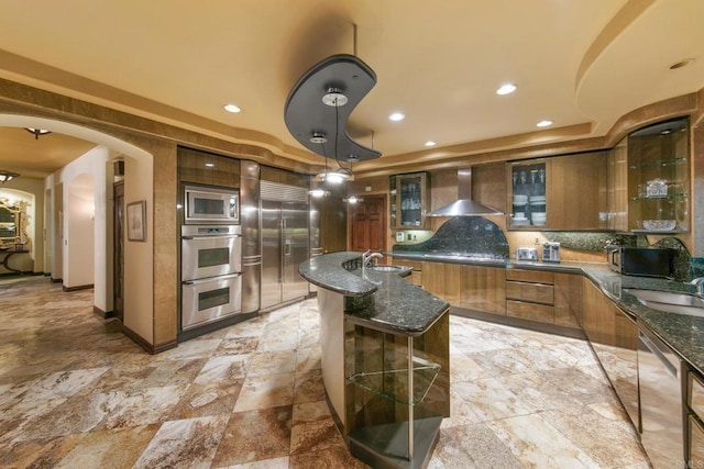 kitchen with sink, wall chimney exhaust hood, hanging light fixtures, and built in appliances