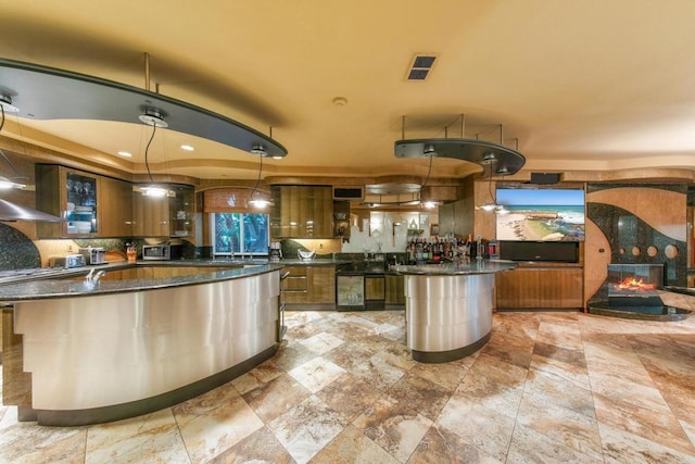 kitchen featuring wine cooler, a fireplace, a kitchen island, hanging light fixtures, and dark stone counters