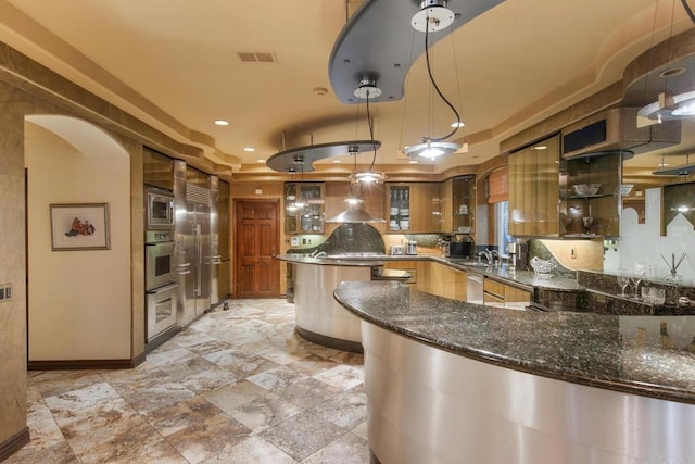 kitchen featuring kitchen peninsula, stainless steel appliances, dark stone countertops, pendant lighting, and sink