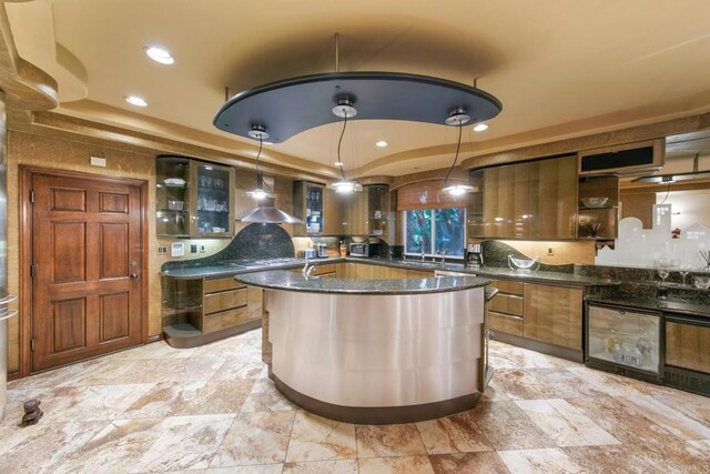 kitchen with hanging light fixtures, wall chimney range hood, a tray ceiling, and dark stone countertops