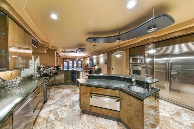 kitchen with sink, built in appliances, dark stone countertops, and pendant lighting