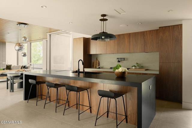 kitchen with pendant lighting, sink, an island with sink, a breakfast bar area, and wood walls