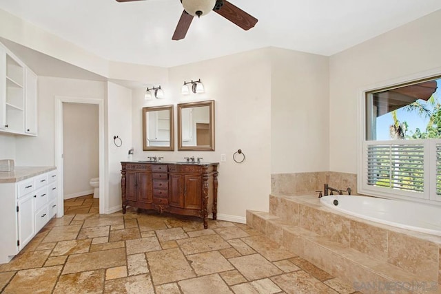 bathroom with vanity, toilet, tiled bath, and ceiling fan