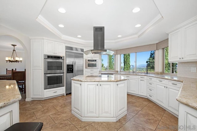 kitchen featuring tasteful backsplash, light stone countertops, appliances with stainless steel finishes, island range hood, and pendant lighting