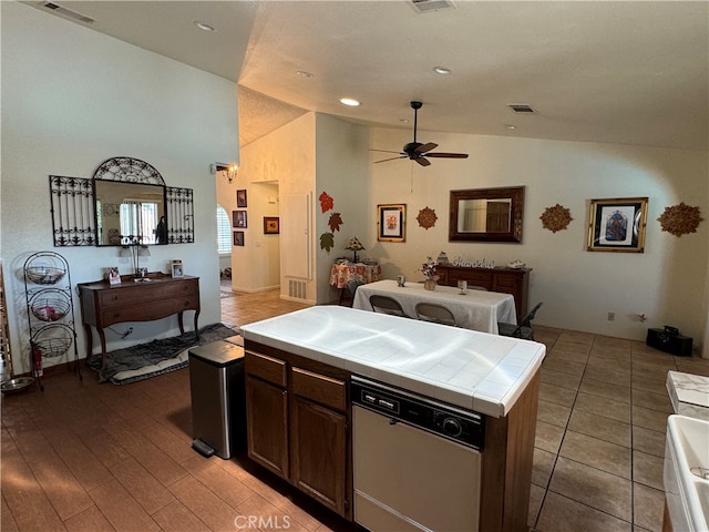 kitchen with dishwashing machine, tile countertops, dark brown cabinets, light hardwood / wood-style flooring, and ceiling fan