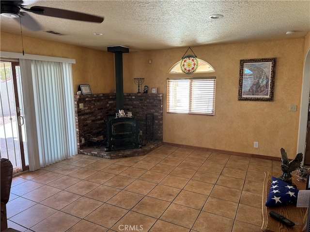 unfurnished living room featuring a textured ceiling, ceiling fan, a wood stove, and plenty of natural light