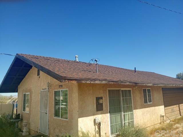 back of property with stucco siding and roof with shingles