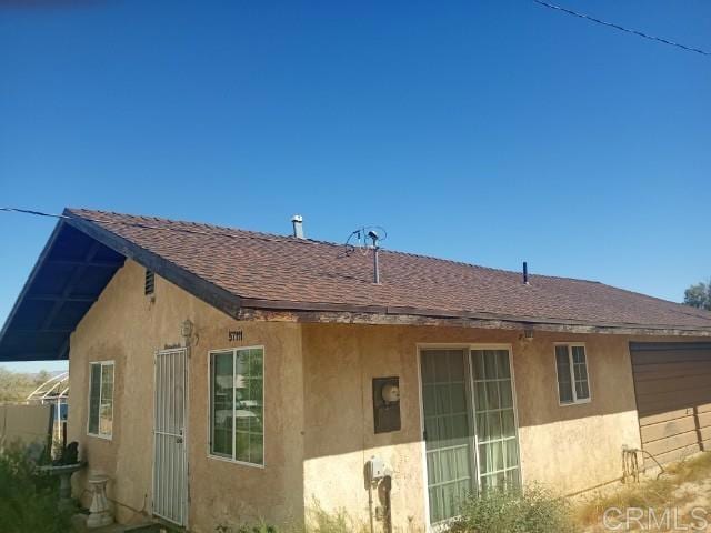 back of property with stucco siding and roof with shingles
