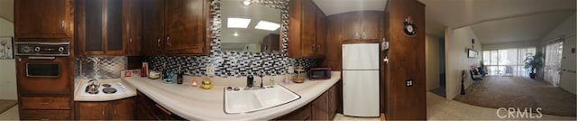 kitchen with decorative backsplash, light countertops, a sink, freestanding refrigerator, and oven