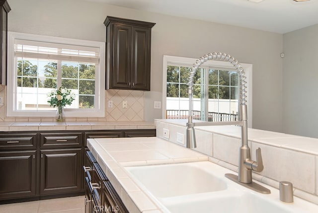 kitchen with dark brown cabinets, light tile patterned flooring, tasteful backsplash, sink, and tile countertops