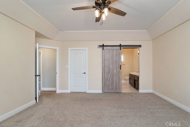 unfurnished bedroom featuring ceiling fan, light colored carpet, ensuite bath, and a barn door