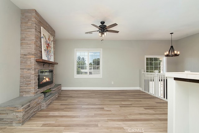 unfurnished living room with a stone fireplace, ceiling fan with notable chandelier, and light hardwood / wood-style flooring