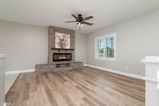 unfurnished living room featuring light hardwood / wood-style flooring, ceiling fan, and a stone fireplace