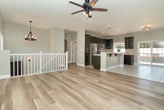 interior space featuring hanging light fixtures, light hardwood / wood-style floors, ceiling fan with notable chandelier, a kitchen bar, and dark brown cabinetry