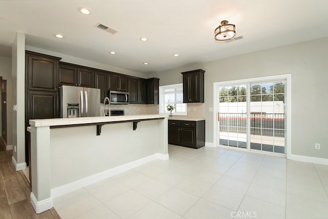 kitchen with dark brown cabinetry, appliances with stainless steel finishes, decorative backsplash, and a breakfast bar