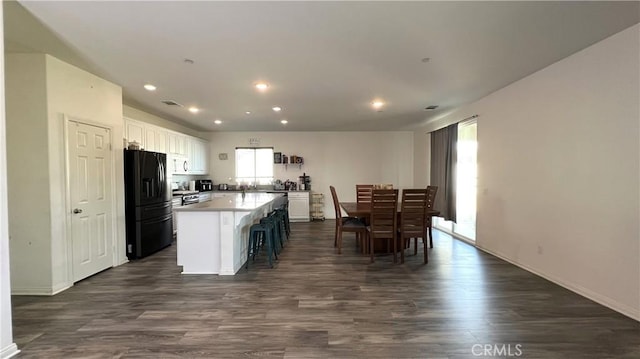 kitchen with black fridge, dark hardwood / wood-style floors, a kitchen breakfast bar, a kitchen island, and white cabinets