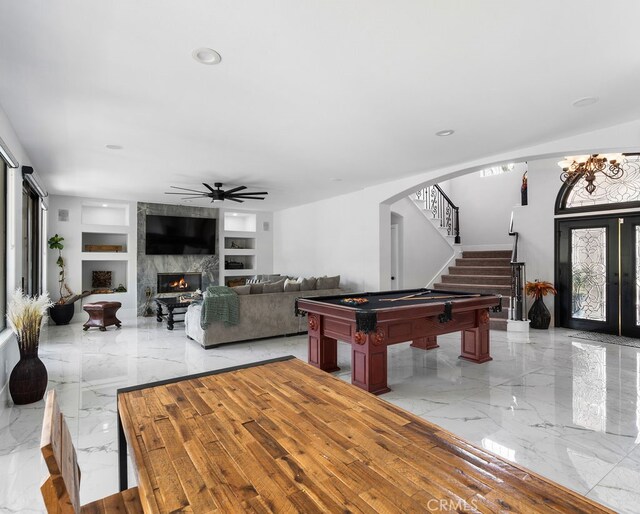 rec room with built in shelves, a high end fireplace, ceiling fan, and a healthy amount of sunlight