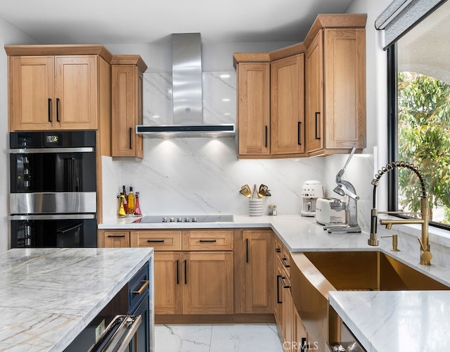 kitchen with light stone counters, wall chimney exhaust hood, black cooktop, stainless steel double oven, and sink