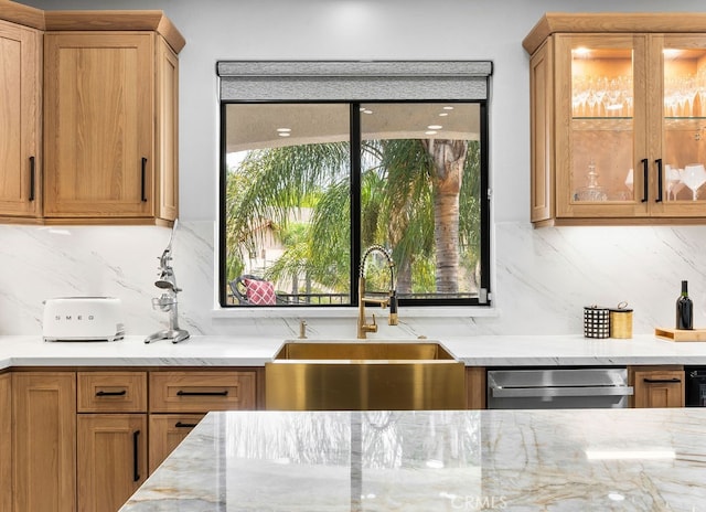 kitchen with backsplash, stainless steel dishwasher, sink, and light stone counters