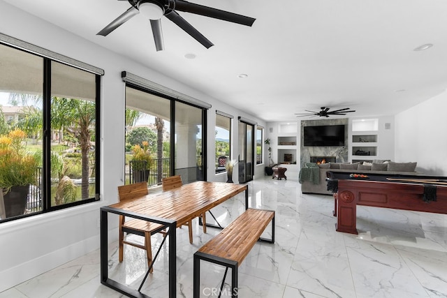 dining space with built in shelves, a fireplace, and ceiling fan