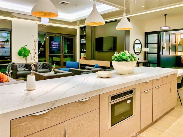 kitchen with light hardwood / wood-style floors, light stone countertops, light brown cabinets, and decorative light fixtures