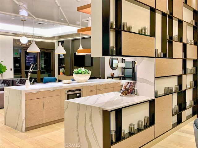 kitchen with light stone countertops, light hardwood / wood-style floors, a large island, and decorative light fixtures