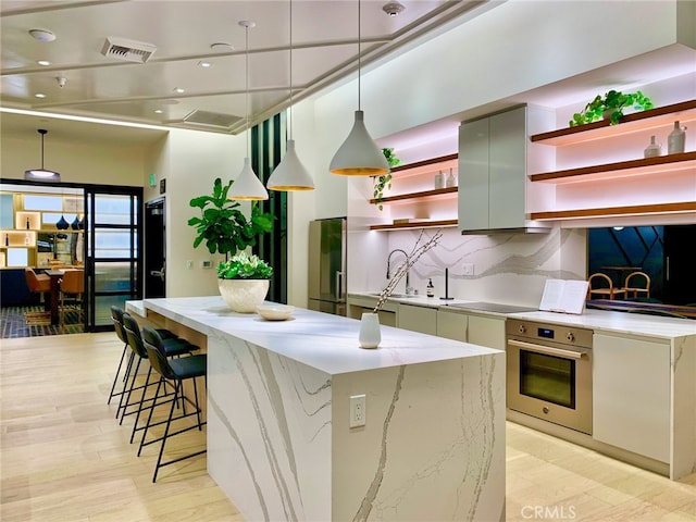 kitchen with tasteful backsplash, hanging light fixtures, a kitchen island, light hardwood / wood-style flooring, and oven