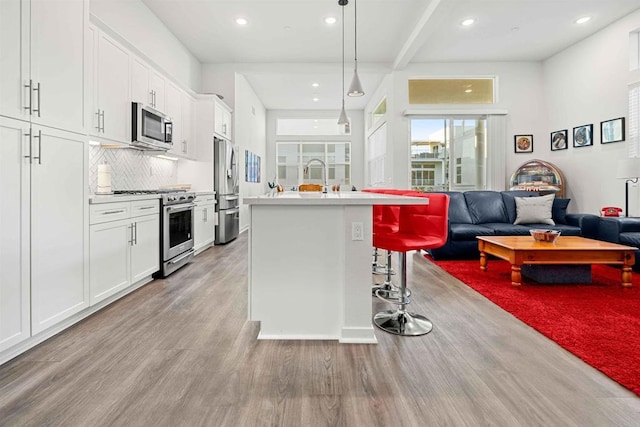 2013 Bravo Loop Unit 5, Chula Vista, CA 91915 - kitchen with stainless steel appliances, open floor plan, light wood finished floors, a kitchen island with sink, and white cabinets