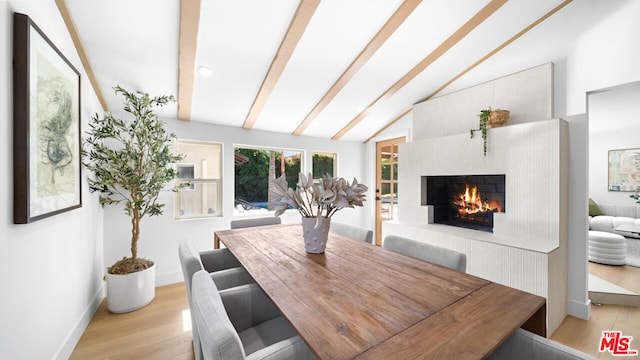 dining space with vaulted ceiling with beams, a fireplace, and light wood-type flooring