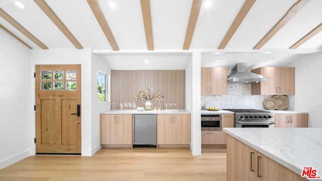 kitchen with wall chimney exhaust hood, light brown cabinetry, tasteful backsplash, refrigerator, and stainless steel stove