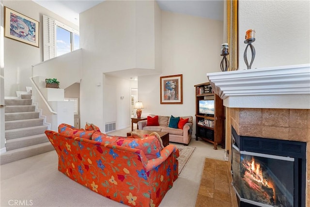 carpeted living room featuring a tiled fireplace and a high ceiling